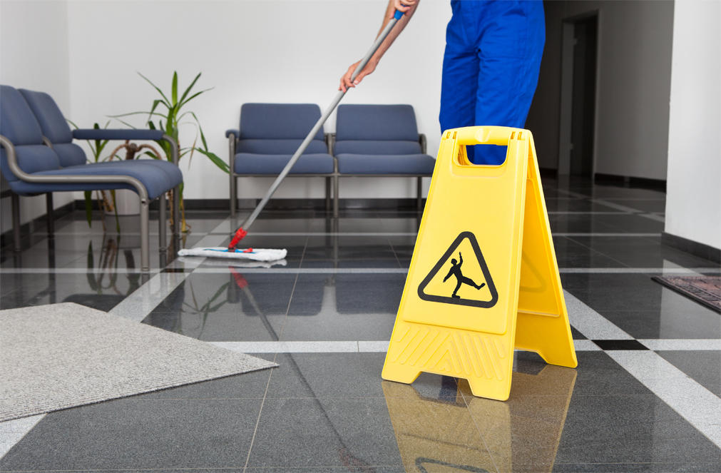 A worker mopping behind a wet floor sign