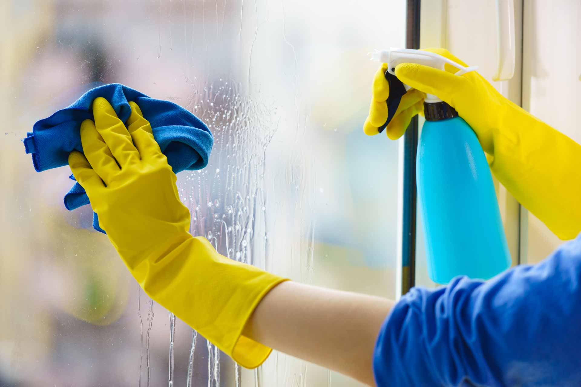 Close up on yellow gloved hands washing window